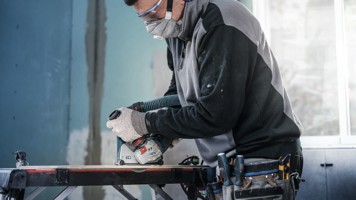 A worker wearing safety equipment cuts wood with a circular saw on a workbench.