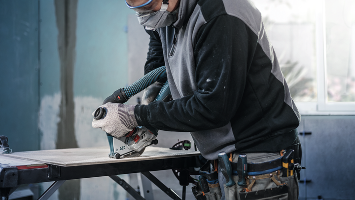 Worker wearing safety equipment cuts a large tile panel using a power saw with dust extraction.