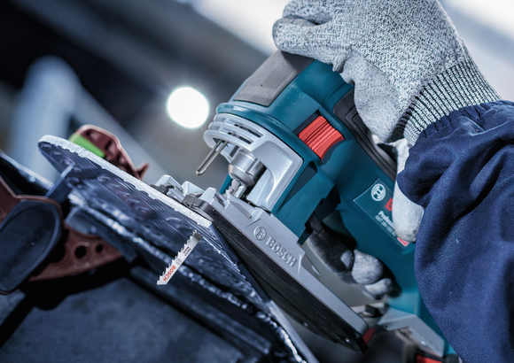 Person wearing safety equipment uses a jigsaw to cut a sheet of material.