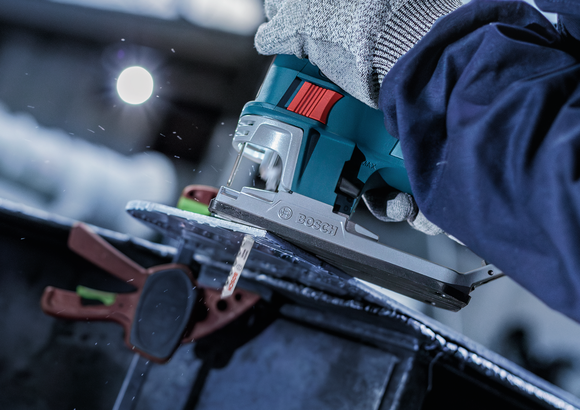 Person wearing safety equipment uses a jigsaw to cut through metal.